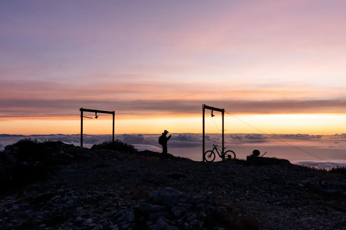 A rider and a bike at sunrise on a summit above the clouds